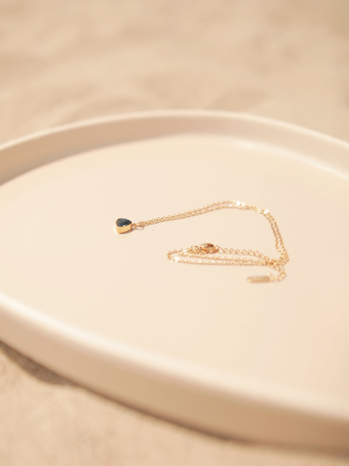 Gold bracelet with a dark green gemstone on a beige plate