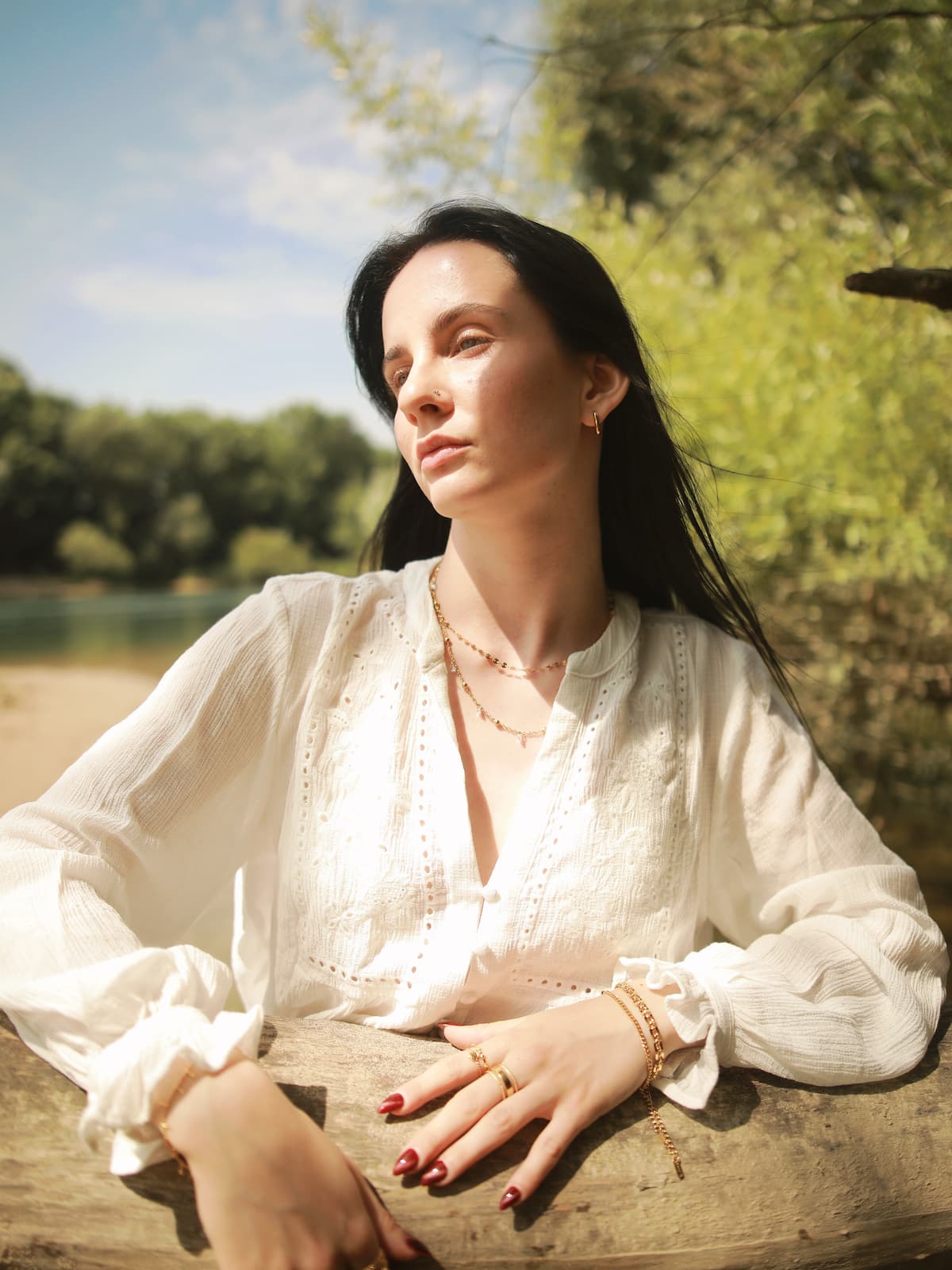 Woman in a white blouse sitting outdoors with trees and sky in the background wearing the Gold Shell Bracelet