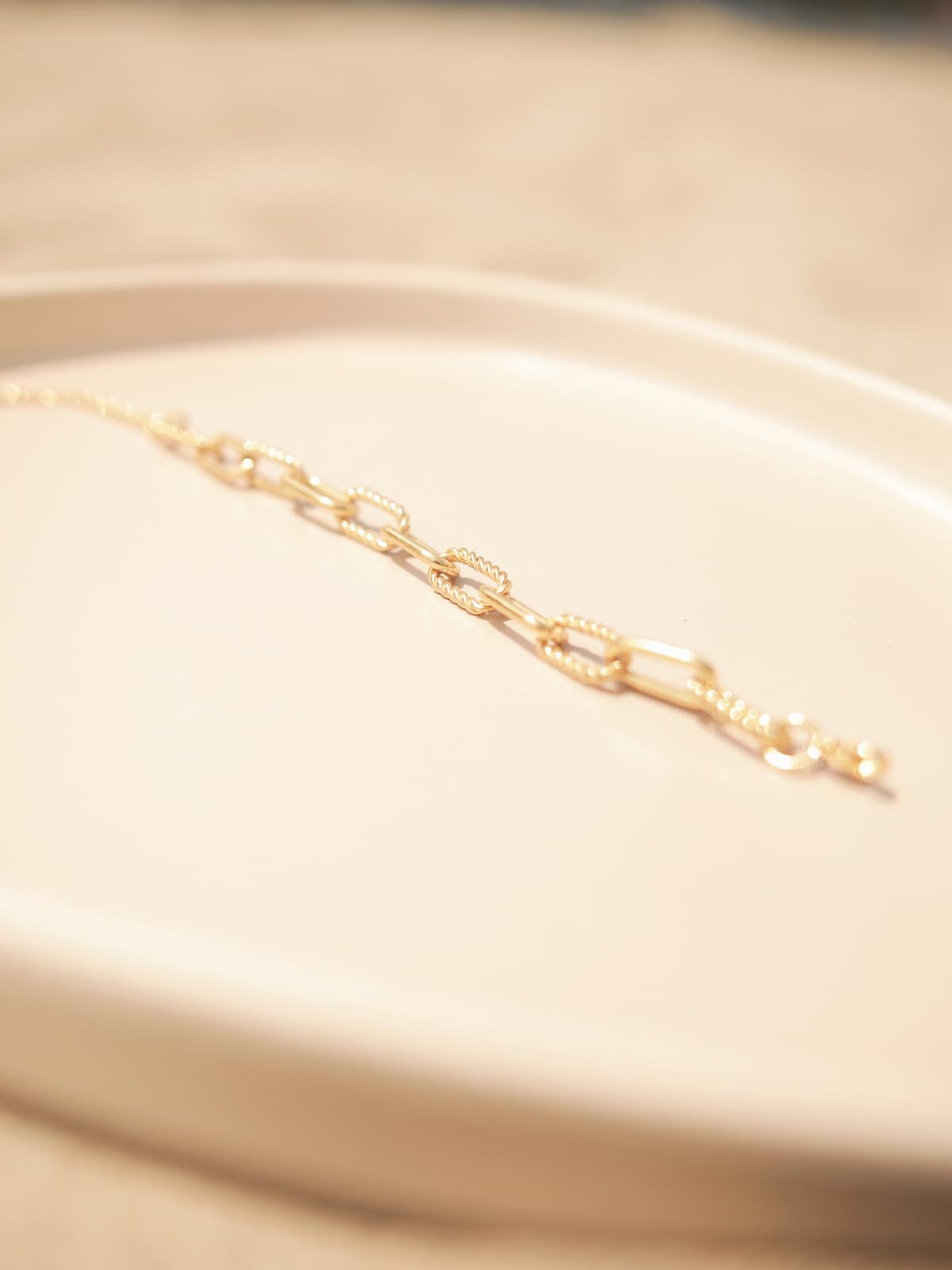 Gold paperclip bracelet on a beige surface