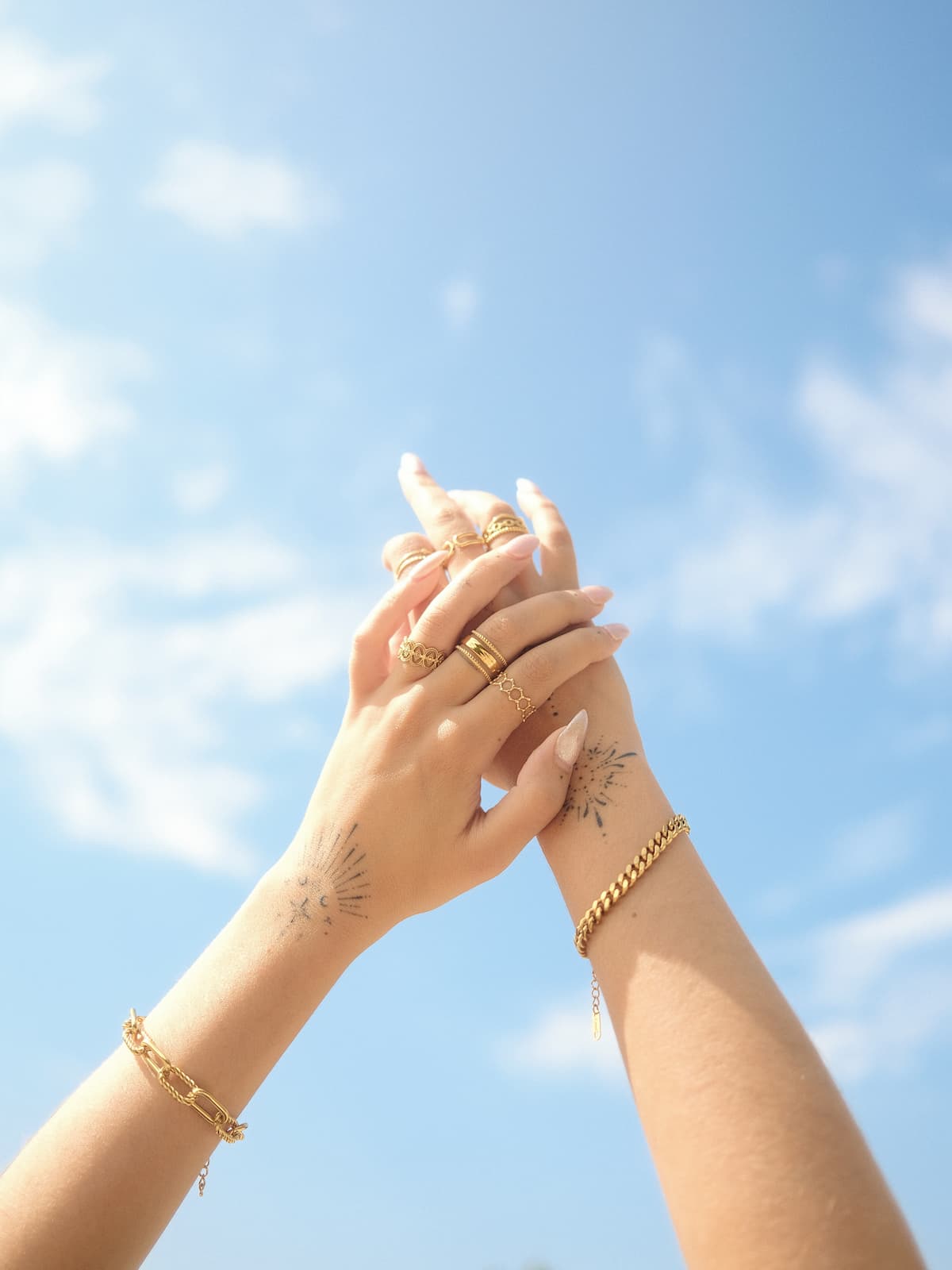 Two hands holding each other against a blue sky with clouds