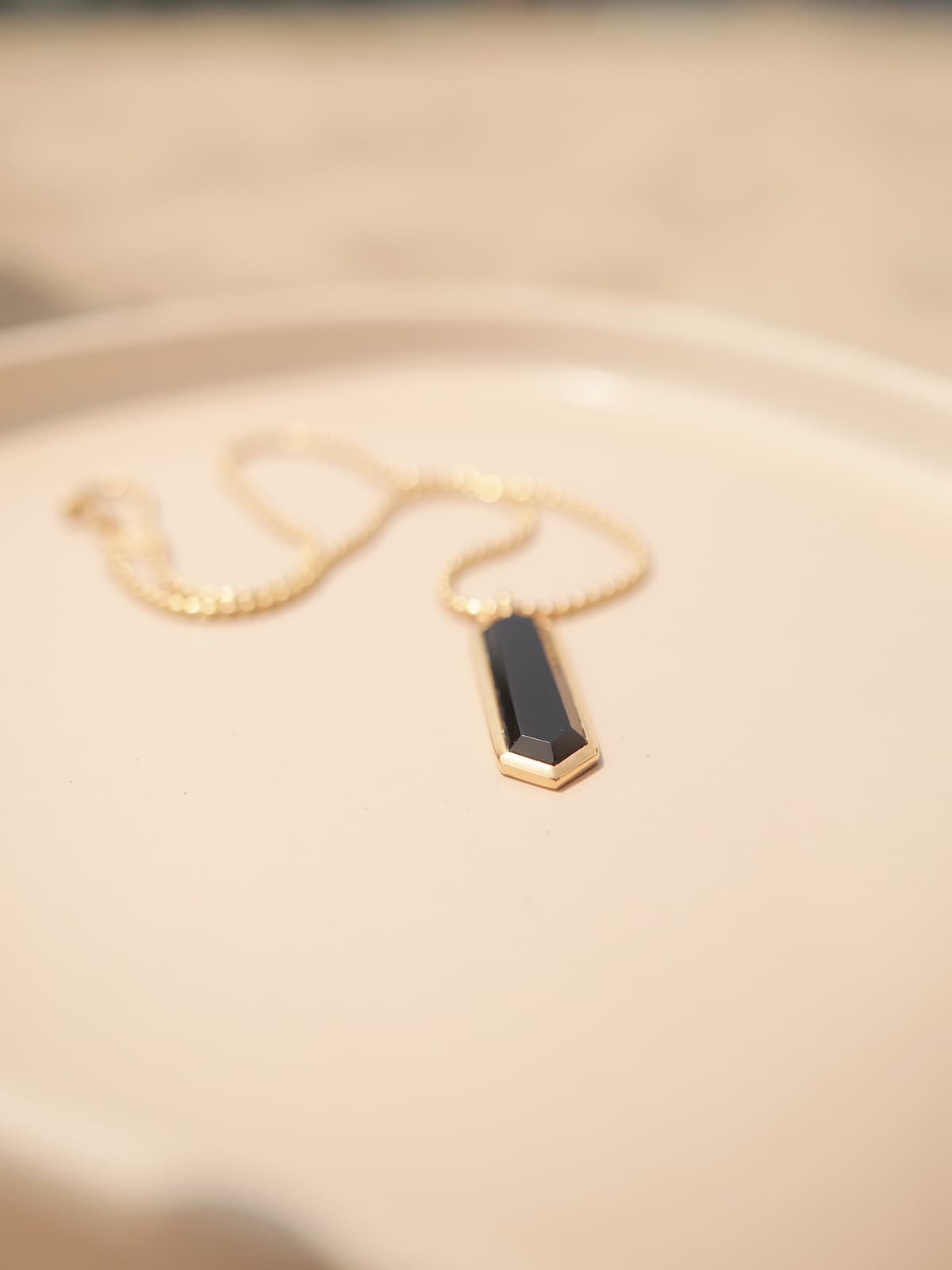 Gold Onyx Necklace with a black pendant on a beige background